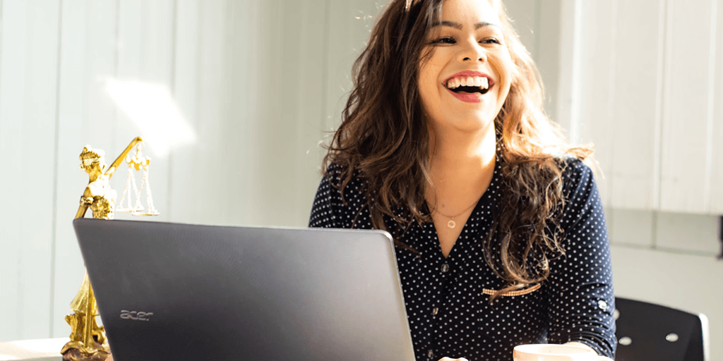 Iloinen nainen tietokoneella, vieressä lakia symboloiva koristepatsas